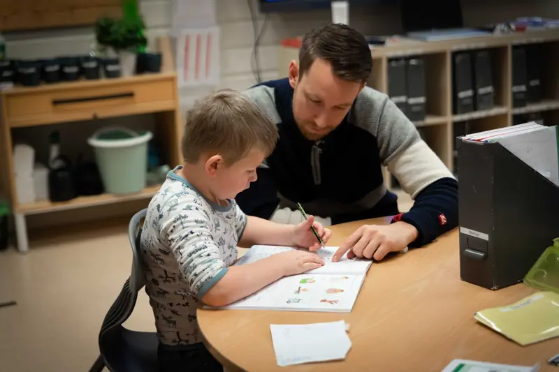 En lærer sitter ved siden av en elev og hjelper med en skriveoppgave