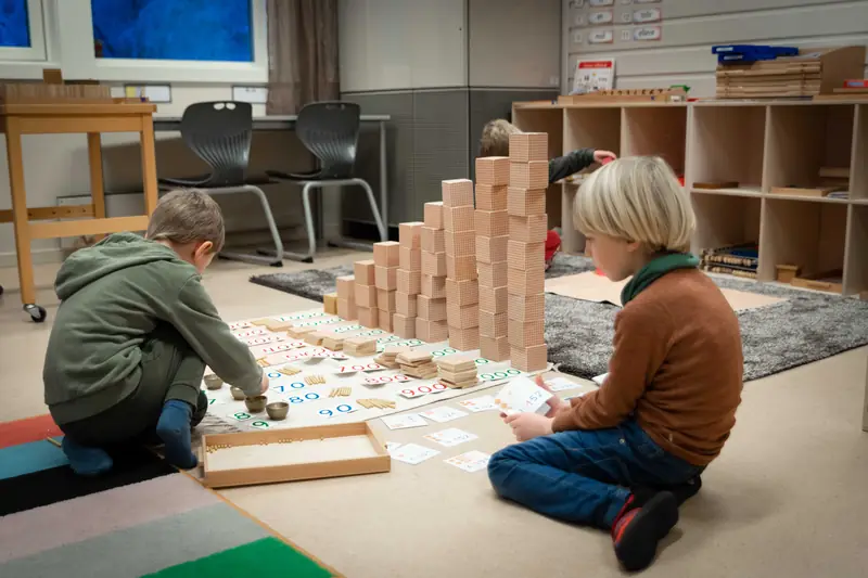 To gutter på gulvet bygger tårn av perlemateriell og legger tallkort
