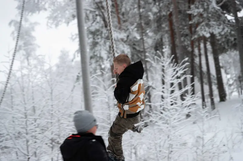 Gutt svinger seg i en tauhuske i snødekt skog